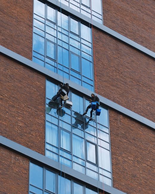 A multi-story residential building constructed from red brick with decorative stone accents, featuring large sash windows, some with white frames, and small balconies with wrought iron railings. The e