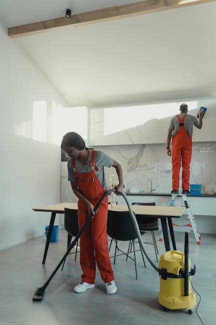 Two professional cleaners from Knightsbridge Cleaner are performing surface cleaning in a modern living room. The cleaner on the left is using a vacuum cleaner on the wooden floor, which appears to be