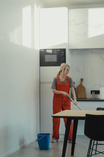 Three professional cleaners from Knightsbridge Cleaner, dressed in grey shirts and orange overalls, are performing surface cleaning in a modern living room. They are equipped with vacuum cleaners and